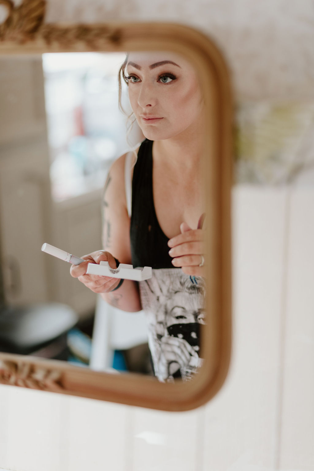 A bride applies makeup, focusing intently while looking into a mirror.