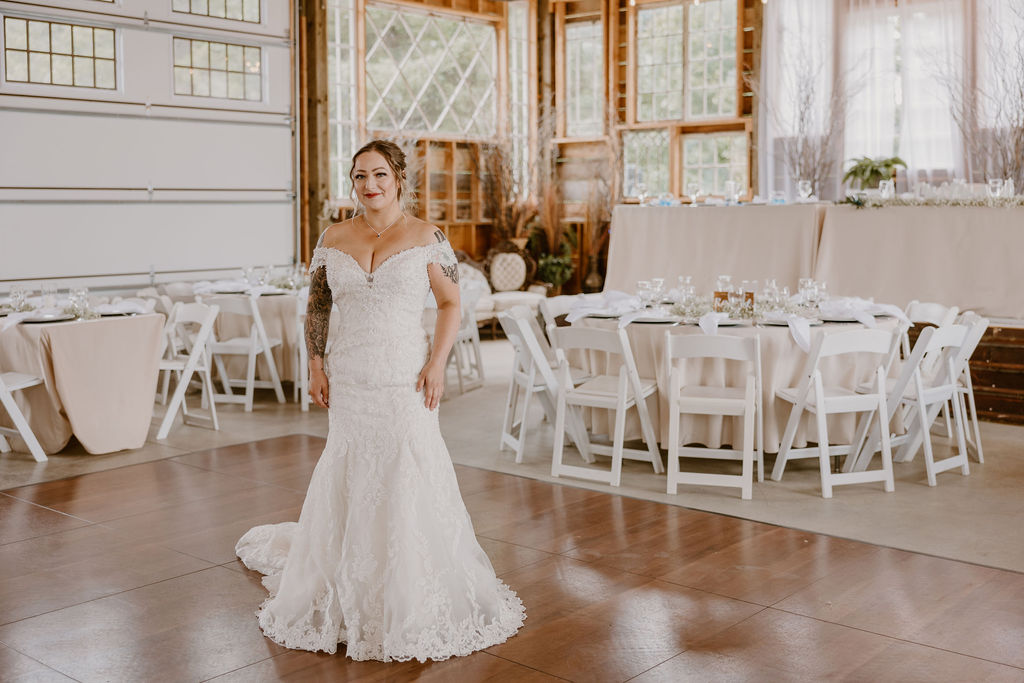 The bride stands inside the reception area, wearing her wedding dress and smiling.