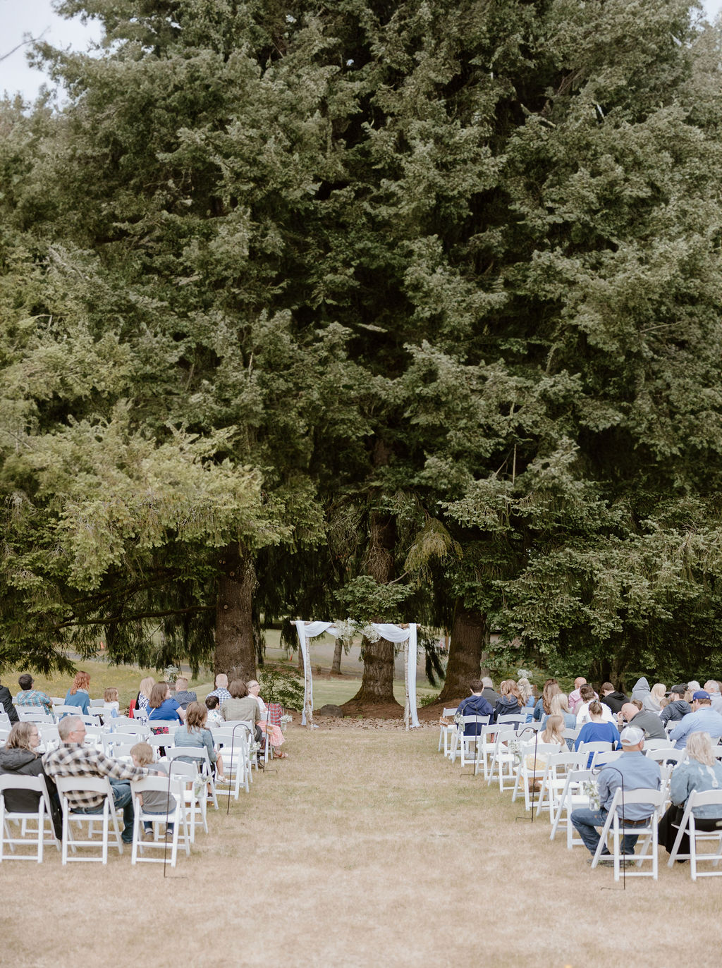 Outdoor wedding ceremony setup with rows of white chairs and a rustic arch.