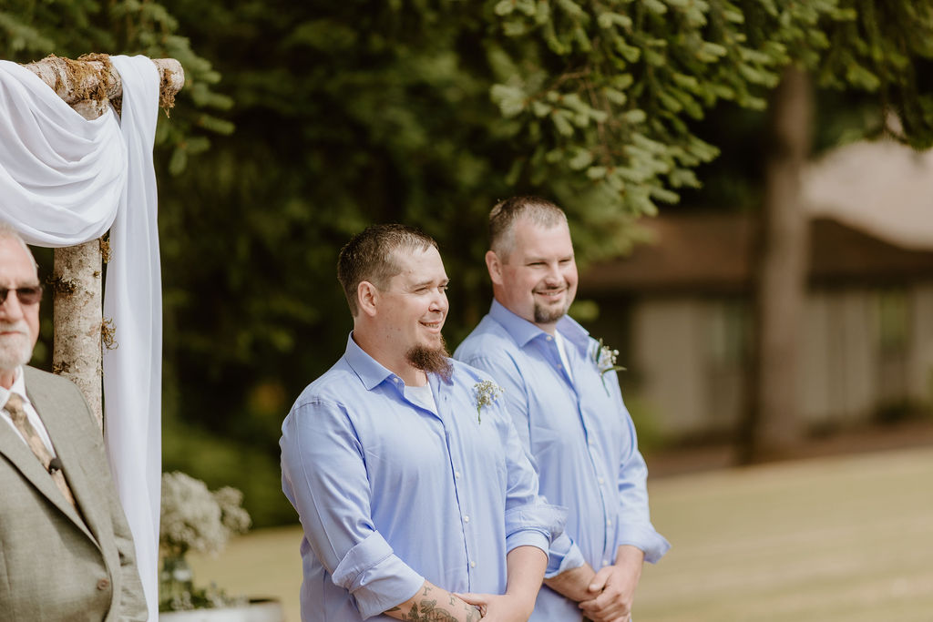 The groom waits at the altar with his best man, smiling in anticipation.