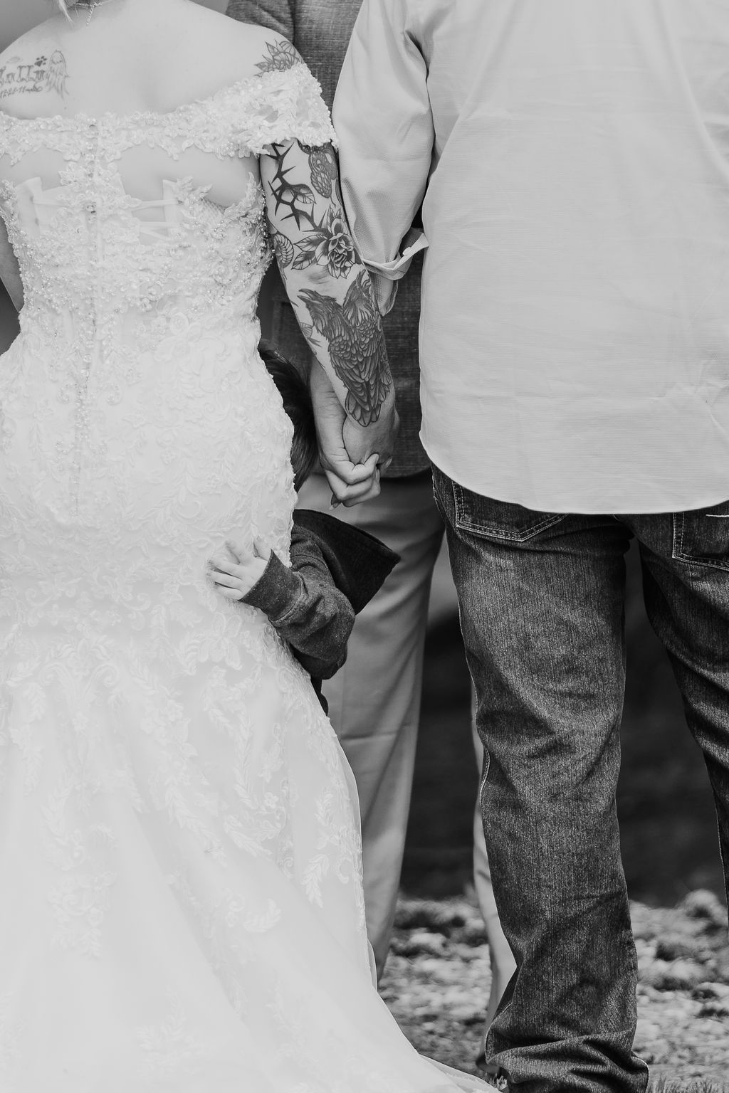 A young child peeks from behind a bride's wedding dress, holding hands with the couple.