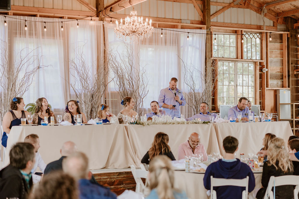 The wedding party laughs and enjoys the speeches at the head table during the reception.