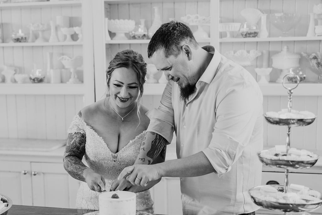 A bride and groom cut their wedding cake together, sharing a joyful and sweet moment.
