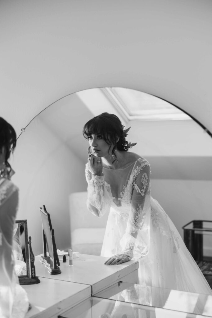 A bride applies the last touch up of her lipstick in a circular mirror in her bridal suite