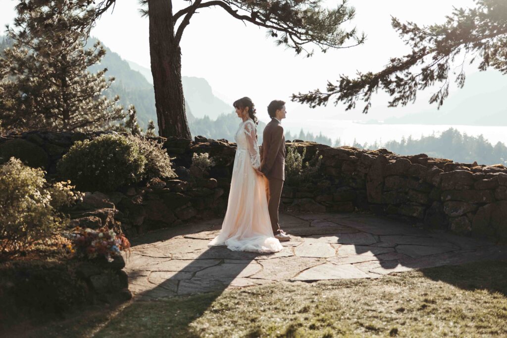 Two female brides holding hands on a cliffside during a romantic Columbia River Gorge elopement at sunset