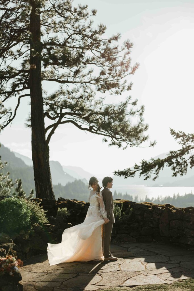 Two female brides holding hands on a cliffside moments before their first look Columbia River Gorge elopement at sunset.