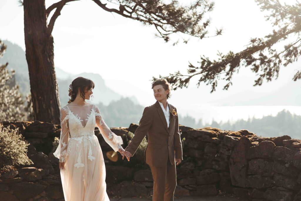 Romantic candid of two female brides turning to see each other for the first time with the columbia river mountains softly blurred in the background