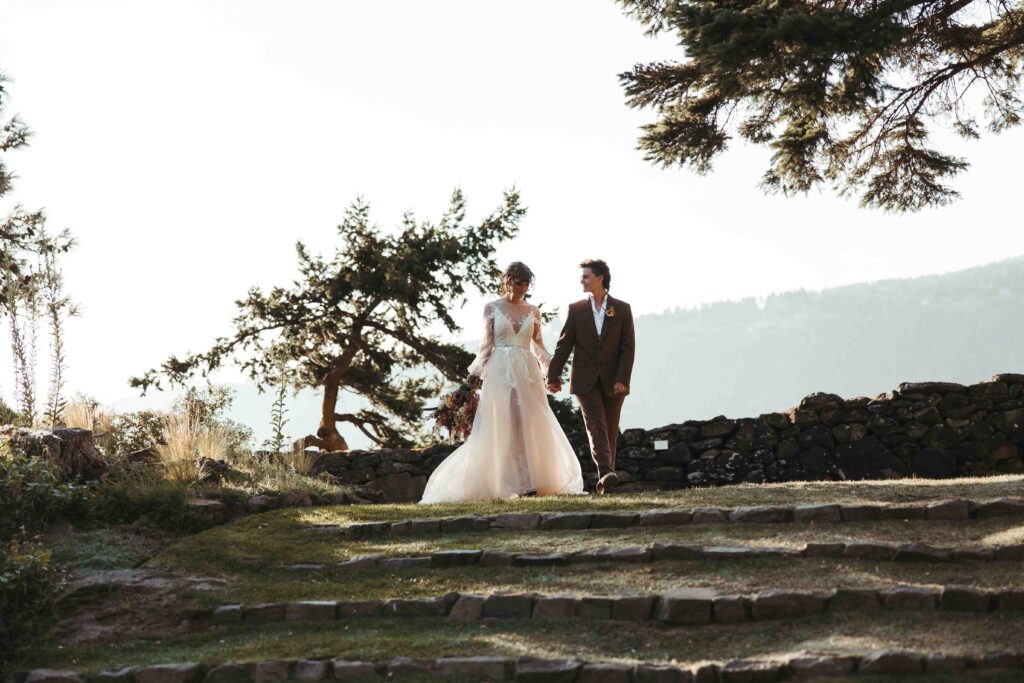 Same-sex couple walking hand in hand along a beautiful stone pavillion with golden-hour light in the Columbia River Gorge