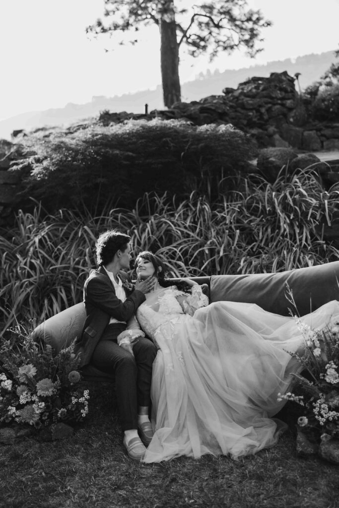 Two female brides hold each other on an elegant couch in a field of ferns during their romantic columbia river gorge elopement
