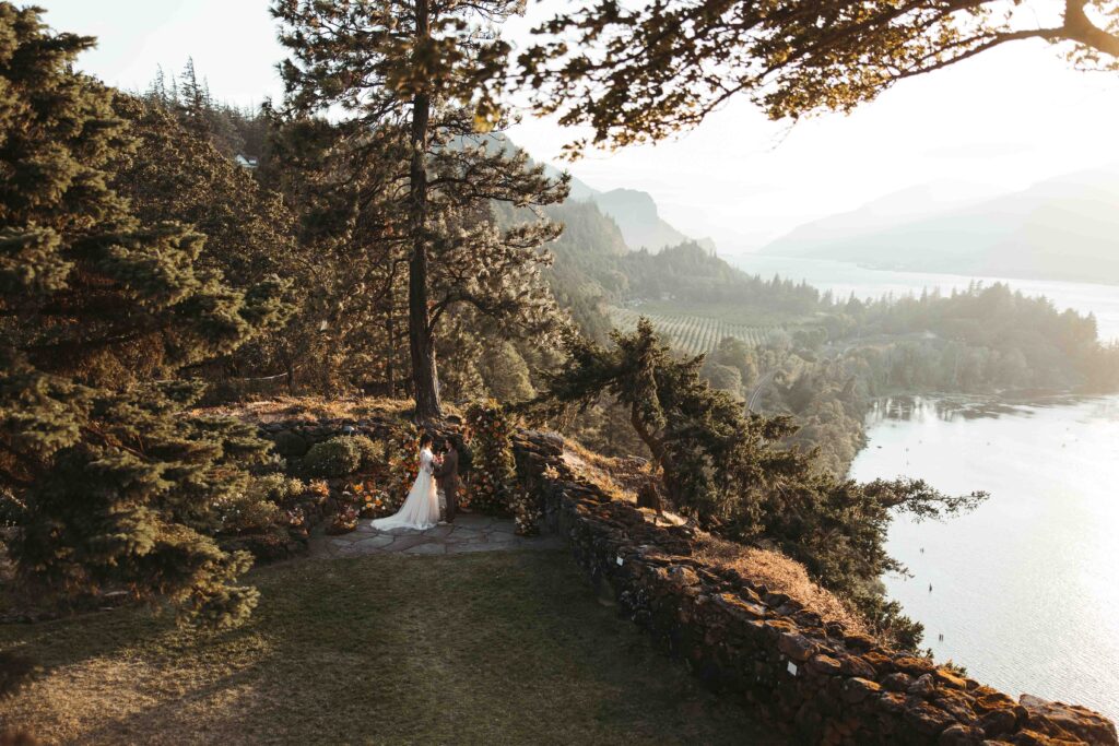 Wide shot of two brides posing in front of their flower arch in the Columbia River Gorge