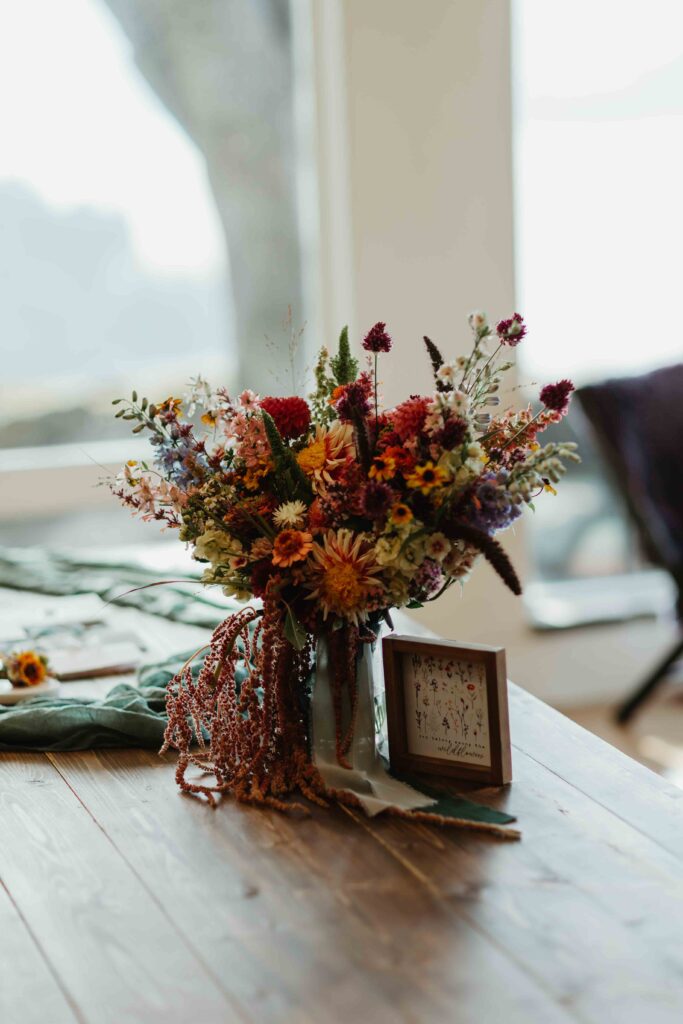a fall-colored bridal bouquet and in memoriam sign placed on a table in front of a large window