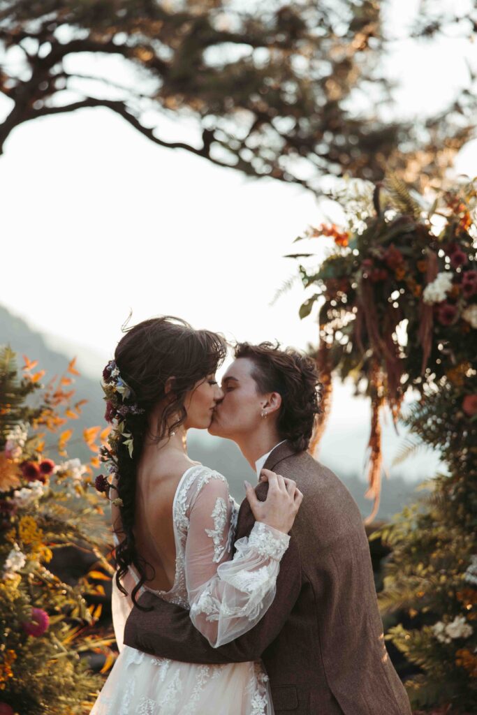 two brides kiss in front of a mountain and a golden sunset