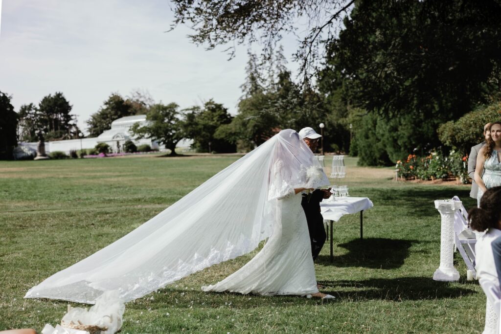a bride walks down the isle with her long veil with her father