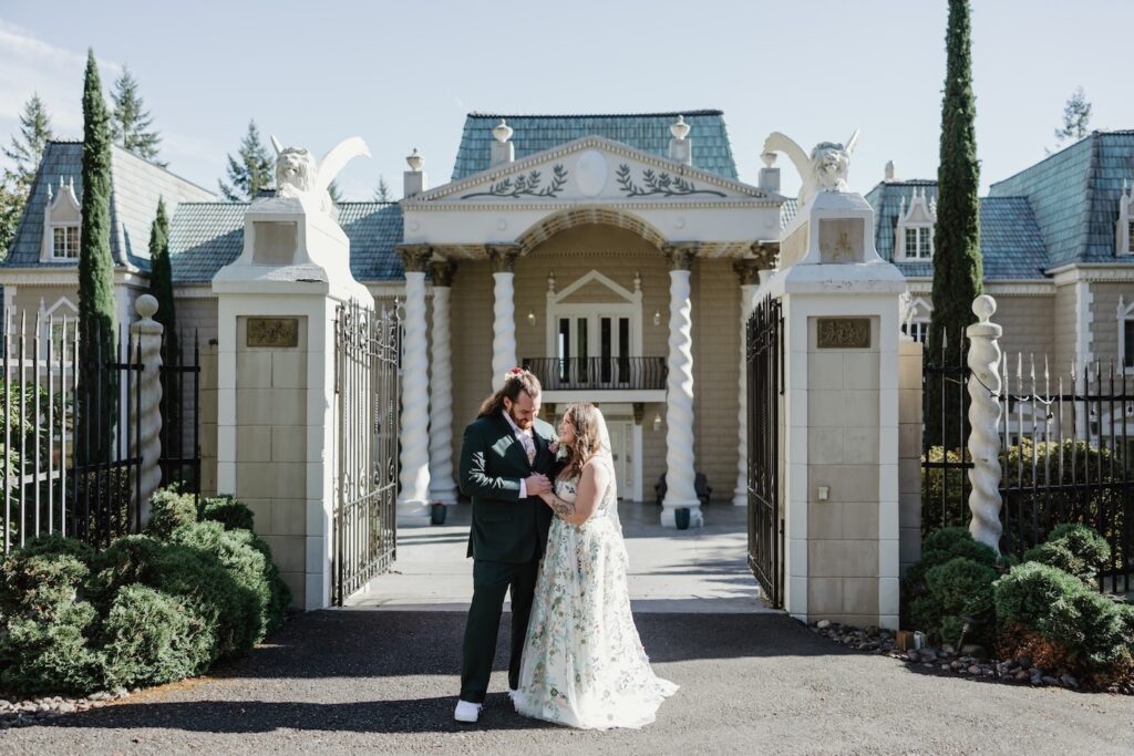 A bride and groom pose in front of the gates of the Empress Estate near Vancouver WA