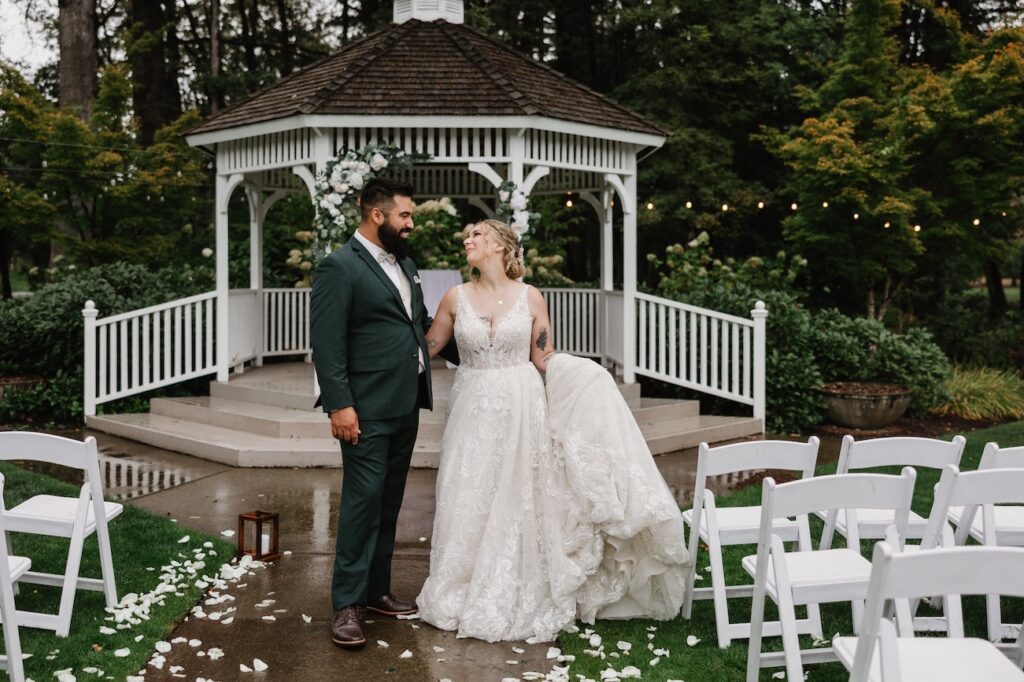 A bride and groom dance together in the rain in front of their ceremony arch and white gazebo in Vancouver WA