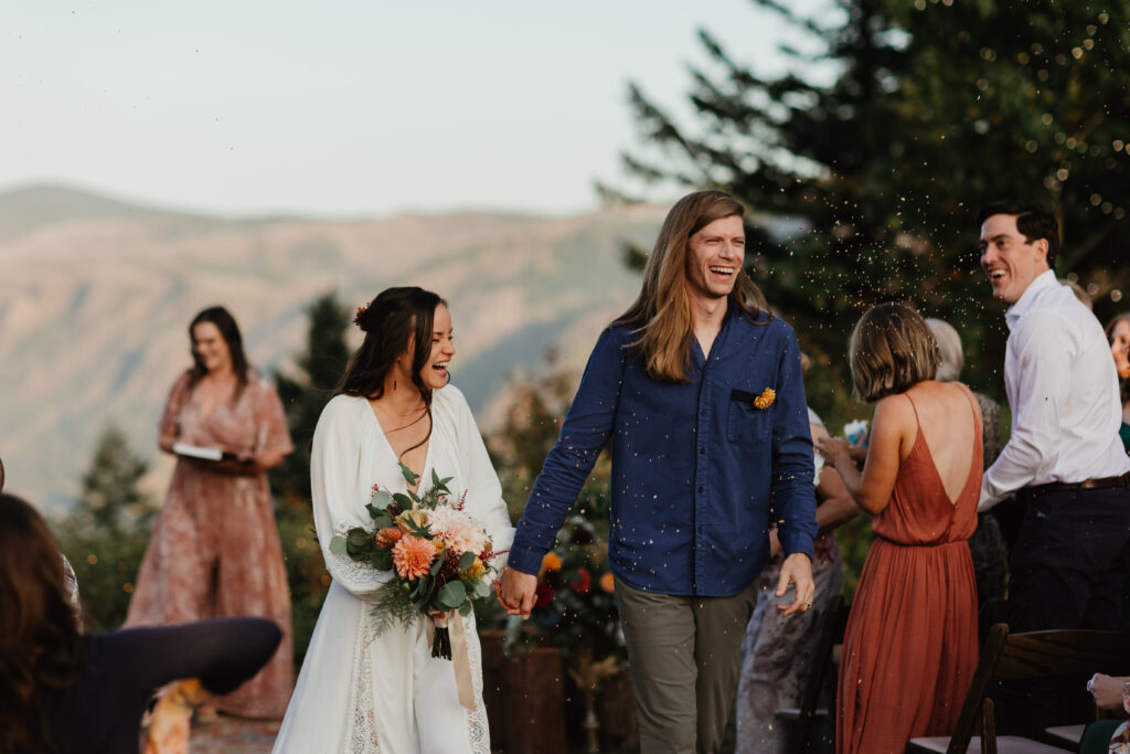 Bride and groom exit their ceremony while their guests cheer at sunset during their wedding in Vancouver WA