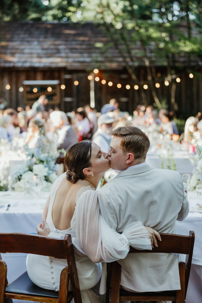 Bride and groom kiss while the crowd cheers during their outdoor reception at Mcmenamins Cornelius Pass Roadhouse
