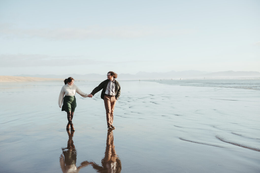 Couple walking along the beach at golden hour near the Peter Iredale wreck Fort Stevens State Park Oregon