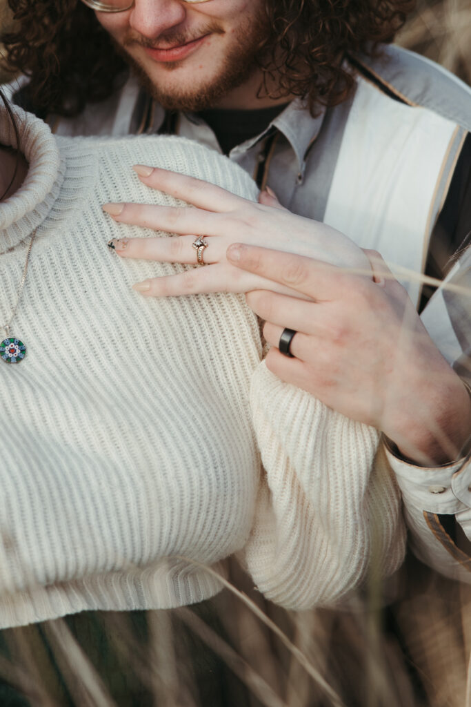 Engaged couple holds hands and shows off their engagement rings at the Oregon Coast