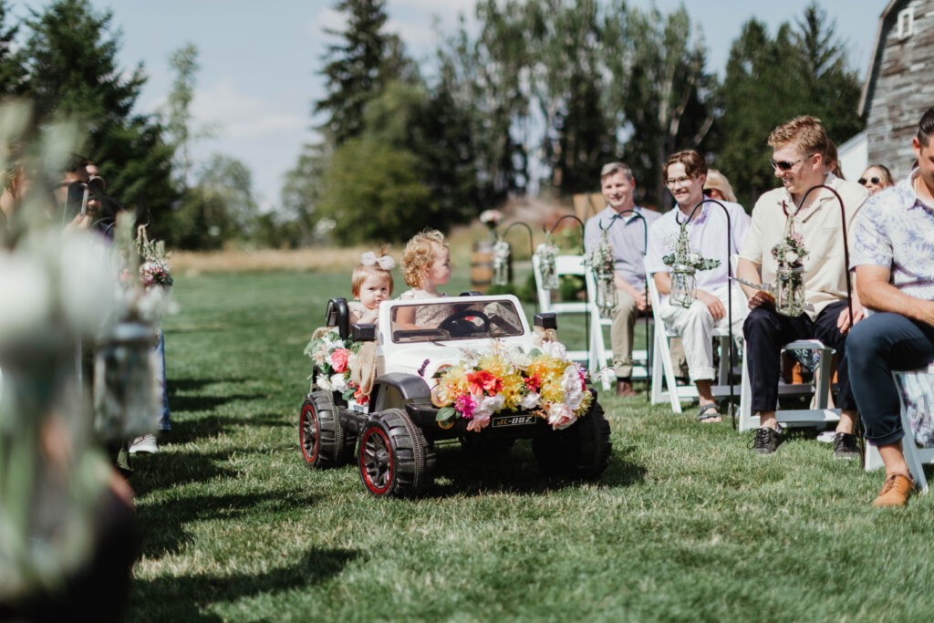 Flower girl arriving in electric toy car during wedding processional at Mount Peak Farm Enumclaw Washington