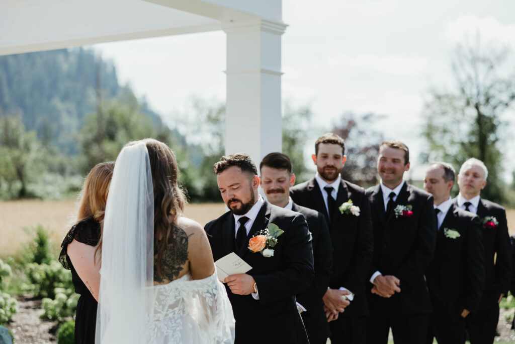 Groom reading his vows to his bride during his wedding ceremony while his groomsmen smile behind him
