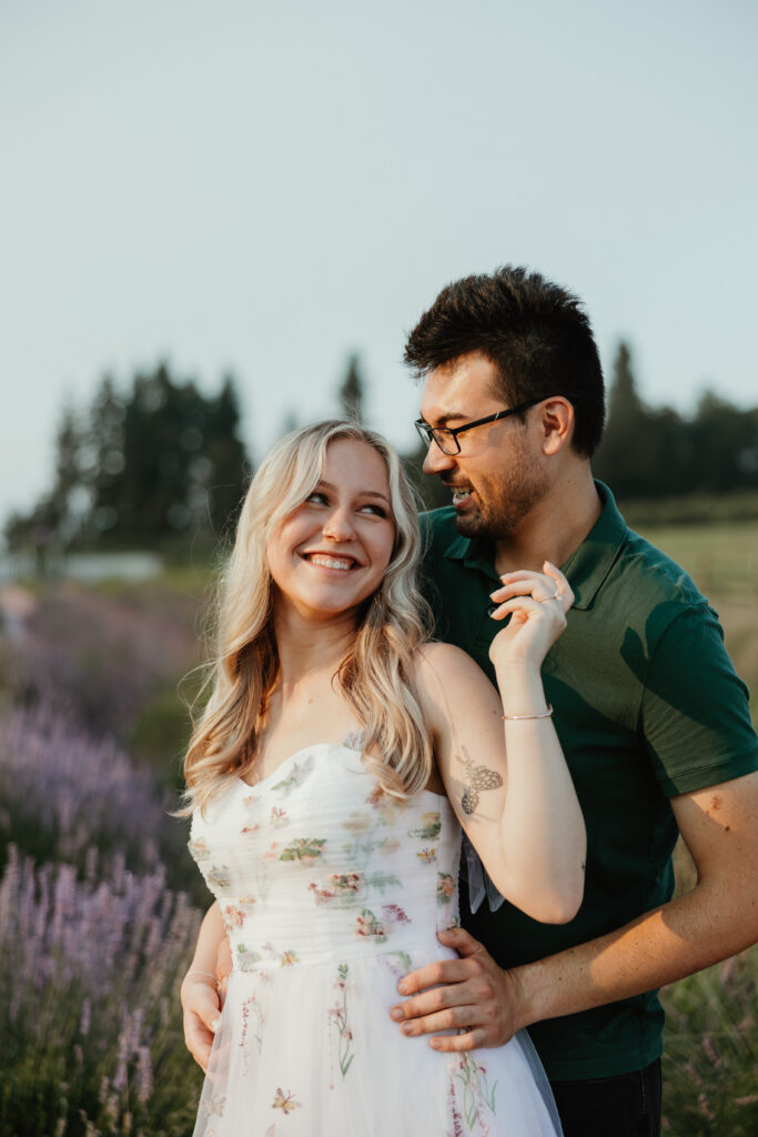 Candid moment of engaged couple smiling in Hood River lavender fields during smoky summer engagement session — The Wickerts Photography