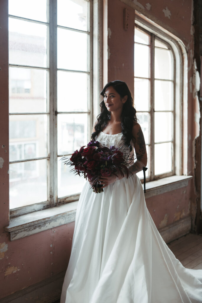 Bride looking out of the window wearing wedding gown before intimate ceremony at The Ruins at the Astor