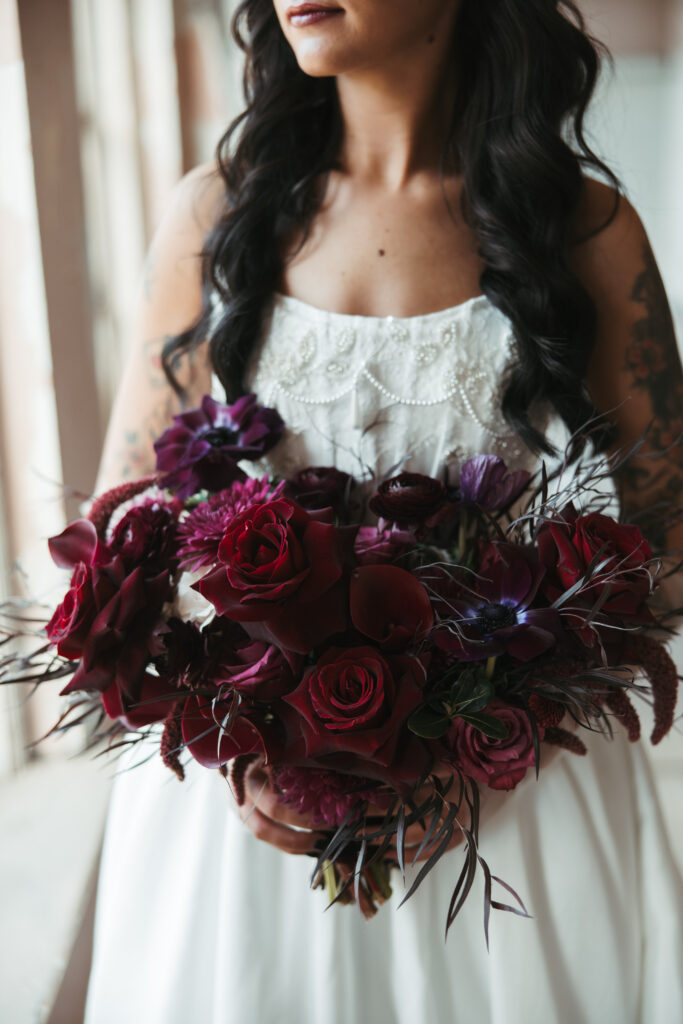 Close-up of bride's hands holding her dark wedding bouquet in soft coastal window light