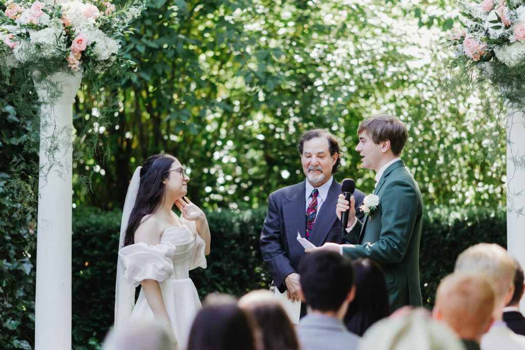 Close-up of bride and groom holding hands during vows at an outdoor summer garden wedding in Salem Oregon