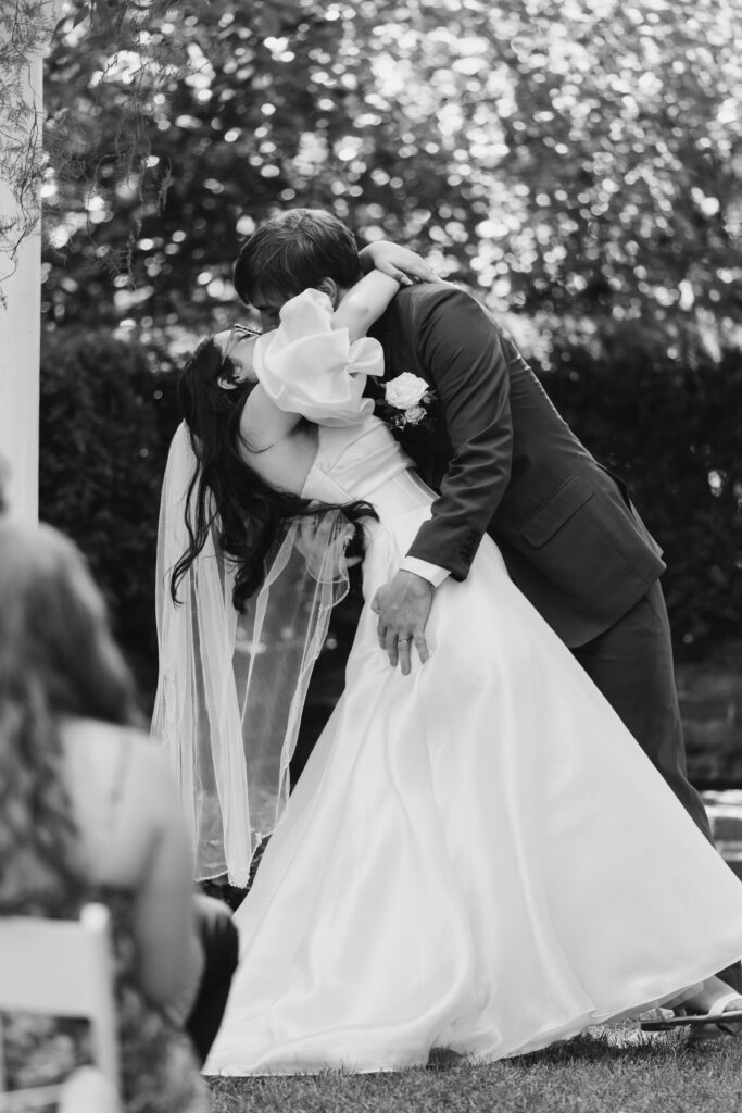 Bride and groom's first kiss surrounded by lush summer florals at Deepwood Museum and Gardens
